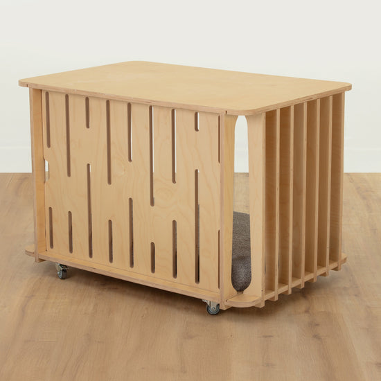 Rear view of the Teddy furniture-style dog crate in birch showing the precision-cut ventilated back panel and lockable castor wheels.